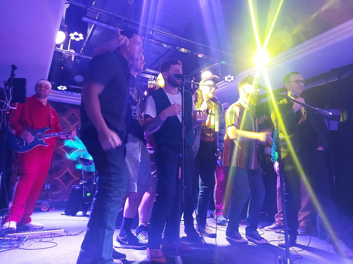 Packed stage group singalong with dramatic blue and purple lighting